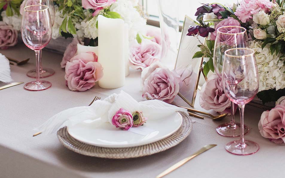 closeup of tablet setting with rattan charger plate, pink roses, and gold cutlery