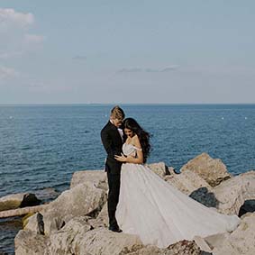 bride and groom embracing on rocks in front of Lake Ontario