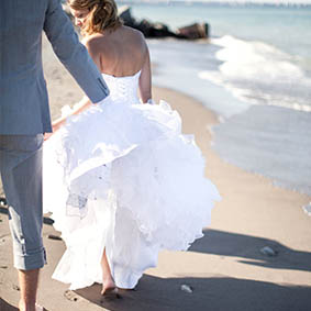 bride and groom walking barefoot on beach in front of lakeview in Hamilton