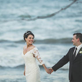 bride and groom holding hands and smiling in front of Lake Ontario