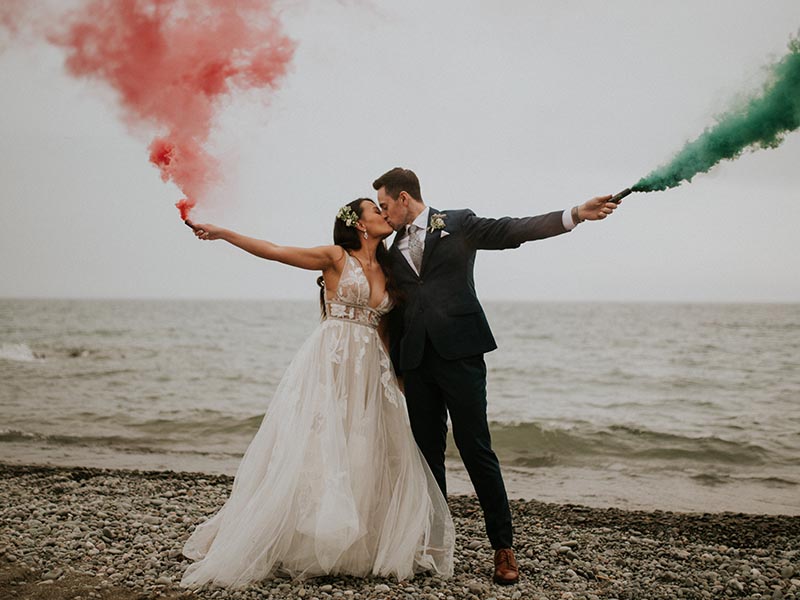 bride and groom kissing while holding green and red smoke bombs