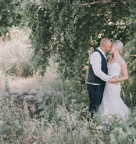 portrait of bride and groom kissing in front of tree