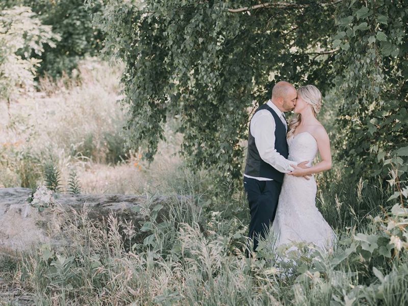 portrait of bride and groom kissing in front of tree
