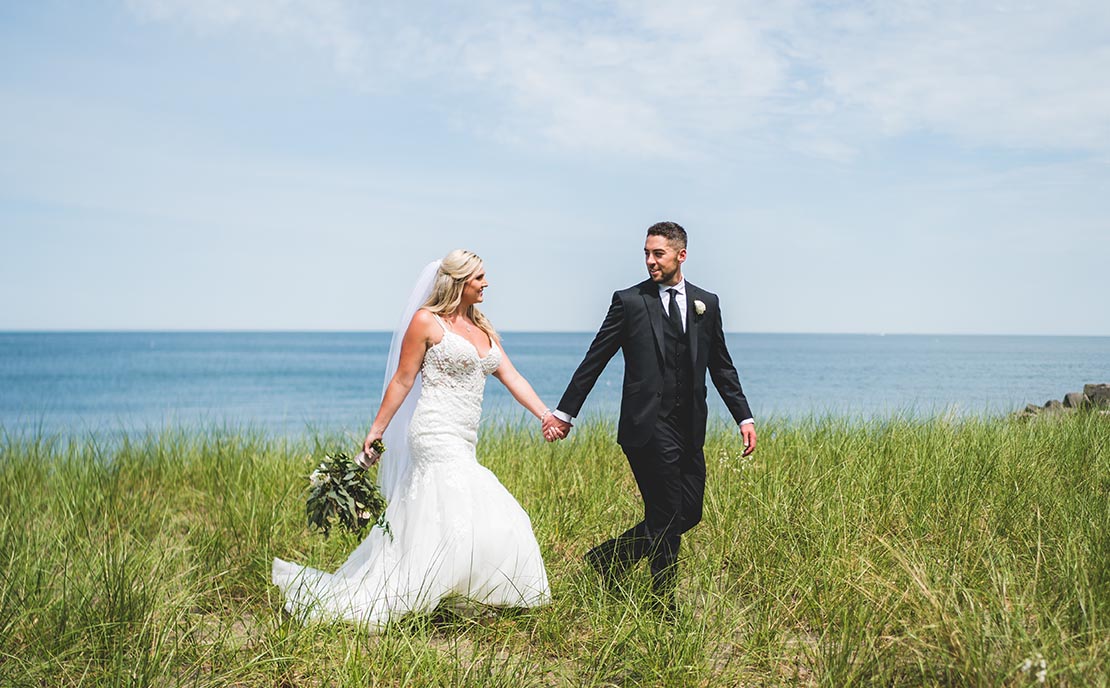 bride and groom walking through grass in front of lake