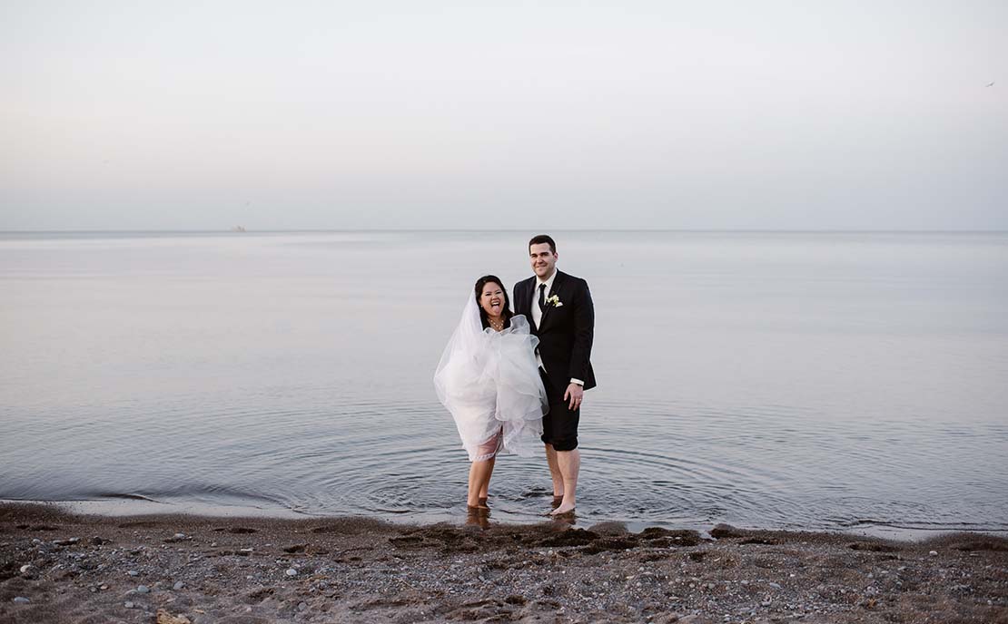 bride and groom laughing standing in the water at beach